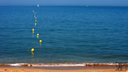 photo de bord de plage avec flotteurs jaunes et voilier lointain